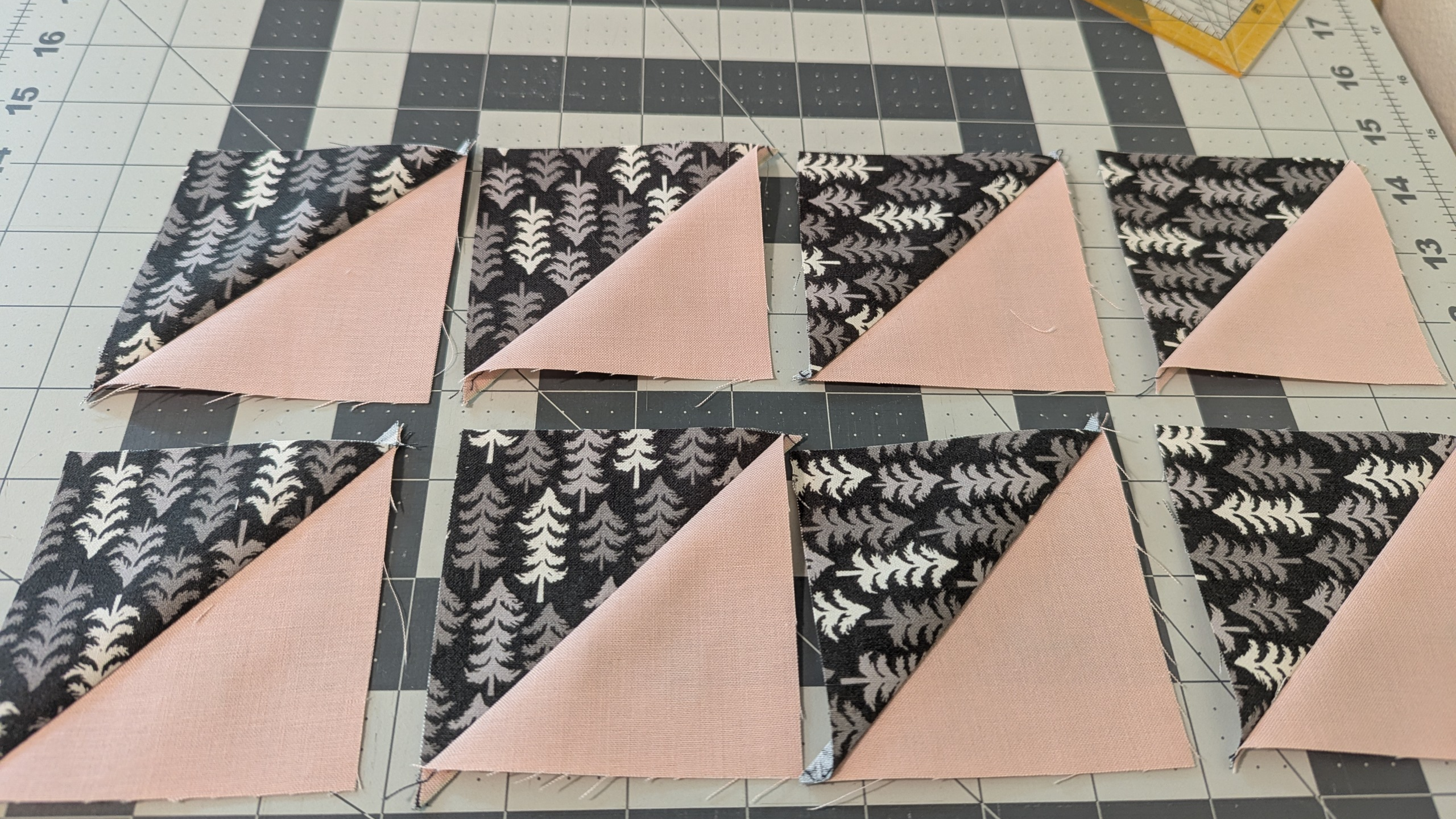 Eight half-square triangle units cut from the same tree-print and solid fabric pairing, laid out on a cutting mat after pressing.