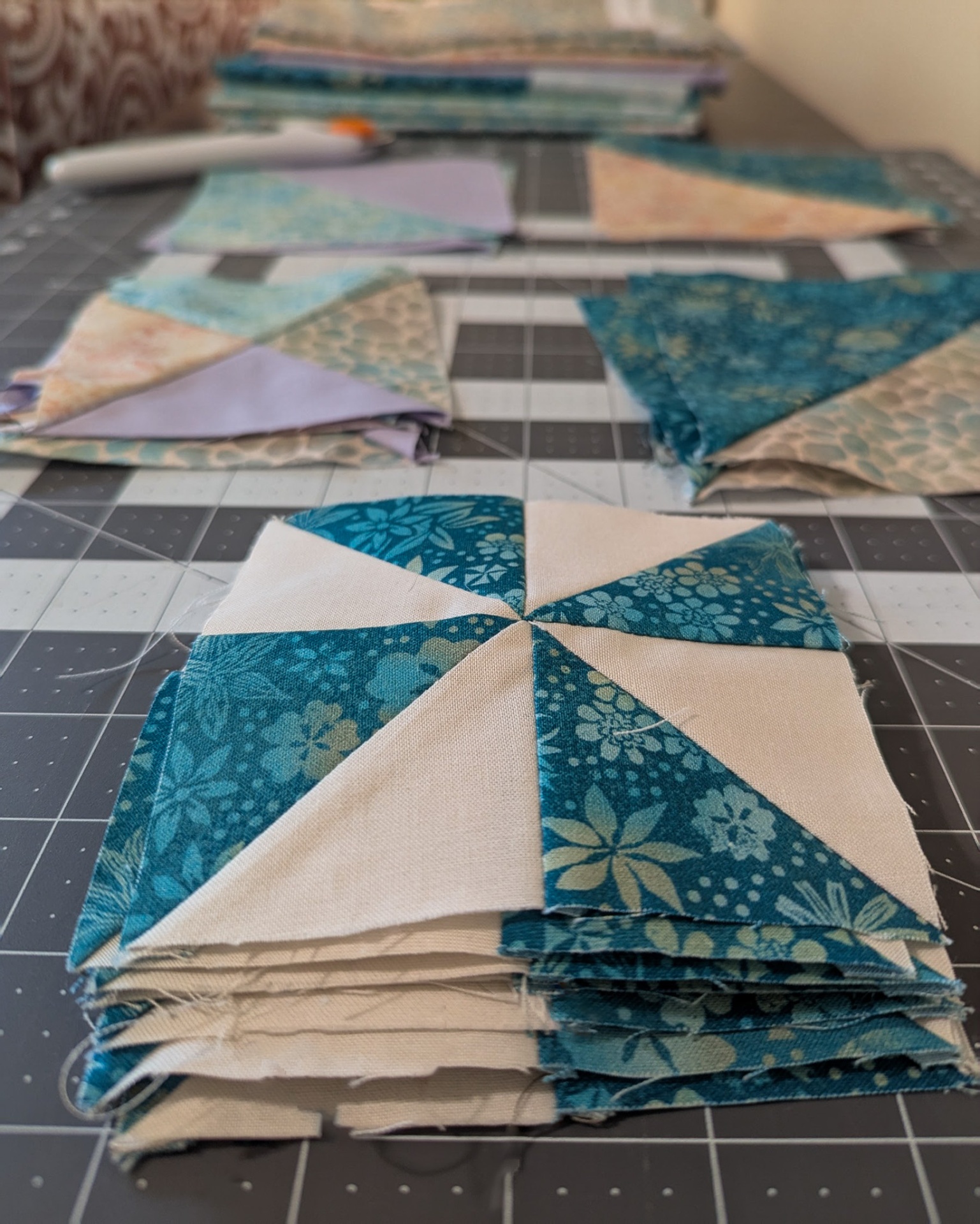 Quilt blocks and fabric pieces arranged on a cutting mat with a rotary cutter